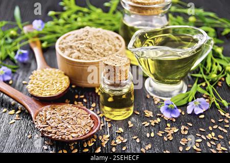 Leinöl in zwei Gläsern und einer Soße Boot mit weißen und braunen Leinsamen in Löffel Mehl in eine Schüssel, Blätter und Blumen auf schwarzem Brett ba Stockfoto