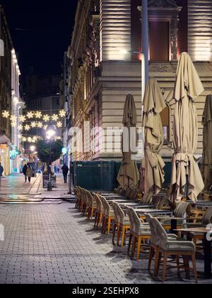 Belgrad, Serbien - 10. Januar 2025: Nächtliche urbane Szene mit Weihnachtsbeleuchtung, geschlossenen Sonnenschirmen und leeren Cafeterstühlen Stockfoto