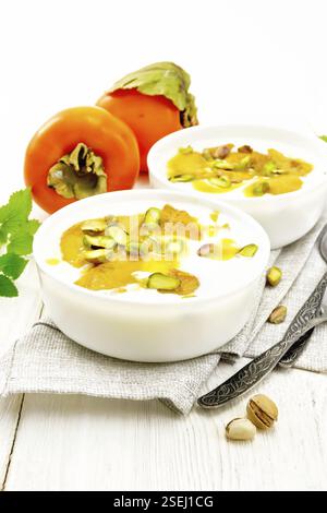 Dessert Joghurt, Dattel und Honig mit Vanille, Kardamom und Pistazien in zwei Schalen auf einem Handtuch, Minze und Löffel auf dem Hintergrund der hellen Holzmöbeln boa Stockfoto