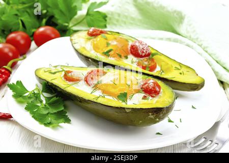 Rührei mit Tomaten in zwei Hälften von Avocado in einer Platte, Handtuch und Gabel auf dem Hintergrund der Holzbretter Stockfoto