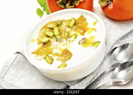 Dessert Joghurt, Dattel und Honig mit Vanille, Kardamom und Pistazien in einer Schüssel auf einem Handtuch, Minze und Löffel auf Holzbrett Hintergrund Stockfoto