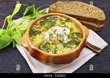 Schweinerippchen Suppe mit Couscous und Spinat in einer Schüssel auf Serviette, Brot auf dunklen Holzplatte Hintergrund Stockfoto