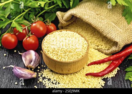 Roher Couscous in einer Schüssel und ein Sack mit Sackleinen, Tomaten, Paprika, Kräutern und Knoblauch auf Holzbrett Hintergrund Stockfoto