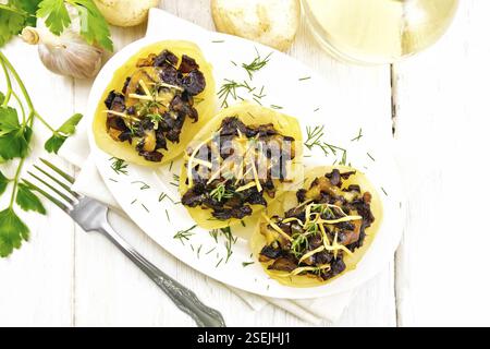 Kartoffeln gefüllt mit Pilzen, gebratenen Zwiebeln und Käse in einer Platte auf Serviette, Pflanzenöl im Dekanter, Petersilie, Knoblauch und einer Gabel auf dem Hintergrund Stockfoto