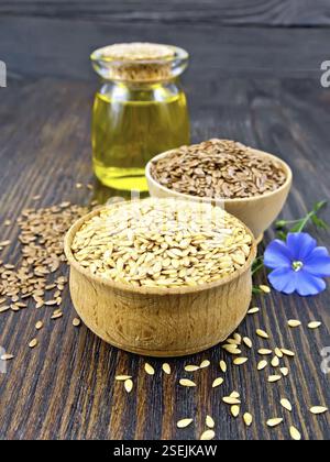 Bettwäsche Samen sind Weiß und Braun in zwei Schalen, Leinöl im Glas und blaue Blume auf einem Hintergrund von dunklem Holz board Stockfoto