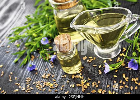 Leinöl in zwei Gläser und eine Sauciere mit Samen, Blätter und Flachs Blumen auf Holzbrett Hintergrund Stockfoto