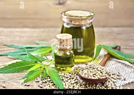 Hanf Öl in zwei Gläser, einen Löffel mit Körnern auf eine Serviette von Sackleinen, Blätter und Stängel von Cannabis vor dem Hintergrund einer alten hölzernen Board Stockfoto