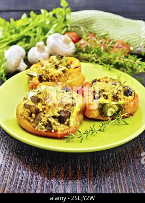 Paprika süss, gefüllt mit Pilzen, Tomaten, Couscous und Käse in einem grünen Schild auf Küchenpapier, Gabel, Petersilie vor dem Hintergrund der Woode Stockfoto