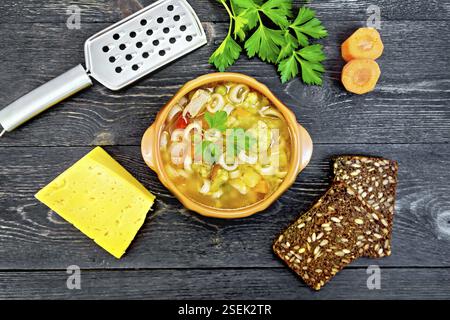 Minestrone mit Fleisch, Sellerie, Tomaten, Zucchini, Kohl, Erbsen, Karotten und Pasta in einem irdenen Schüssel, Käse, reibe auf Schwarz hinterg Stockfoto