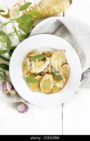 Gebackene Pastinaken mit Gewürzen, Knoblauch und Salbei auf einem Teller auf einem Handtuch auf Holzbrett Hintergrund von oben Stockfoto