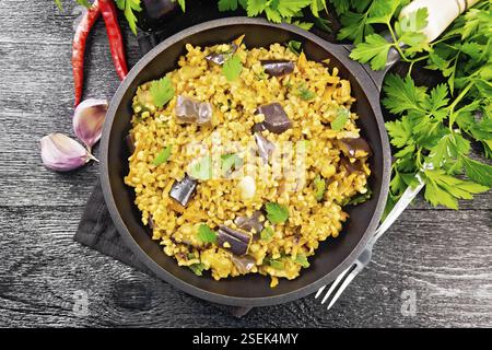 Bulgur mit Auberginen, Karotten, Knoblauch und Zwiebeln in einer Pfanne auf einem Handtuch auf Holzbrett Hintergrund von oben geschmort Stockfoto