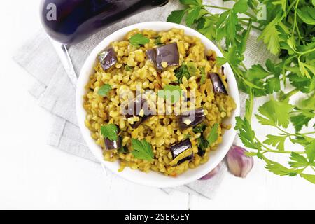 Bulgur mit Auberginen, Karotten, Knoblauch und Zwiebeln in einer Schüssel auf Serviette auf Holzbrett Hintergrund von oben geschmort Stockfoto