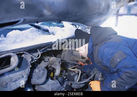 Mann, der am Motor arbeitet, unter geöffneter Motorhaube, umgeben von Schnee Stockfoto