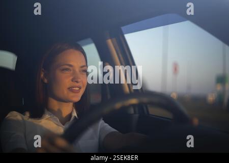 Frau, die am Abend fährt, sich auf die Straße konzentriert, umgeben von Stadtlichtern Stockfoto