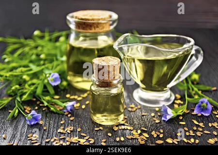 Leinöl in zwei Gläser und eine Sauciere mit Samen, Blätter und Blüten von Flachs auf dunklen Holzplatte Hintergrund Stockfoto