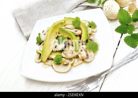 Salat mit Avocado und rohen Champignons, gewürzt mit Zitronensaft und Pflanzenöl mit Minze, Handtuch für die Küche und eine Gabel auf dem Hintergrund der ligh Stockfoto