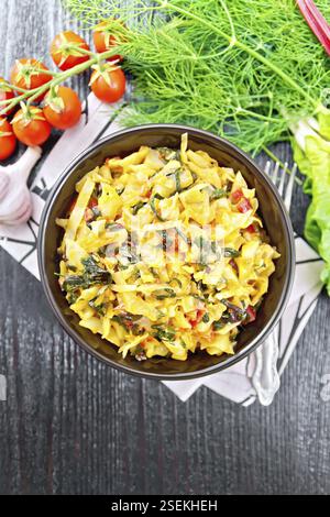 Kohl mit Blattrüben und Tomaten in einer Schüssel auf Serviette, Petersilie, Knoblauch und einer Gabel auf dunklem Holzgrund von oben eintopen Stockfoto