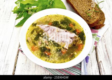 Schweinerippchen Suppe mit Couscous und Spinat in einer Platte auf eine Serviette, Brot auf dem Hintergrund einer Holzplatte Stockfoto