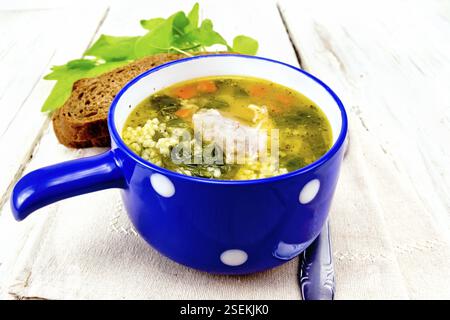 Schweinerippchen Suppe mit Couscous und Spinat in einer blauen Schale auf der Serviette, Brot auf dem Hintergrund des Lichts Holzbrett Stockfoto