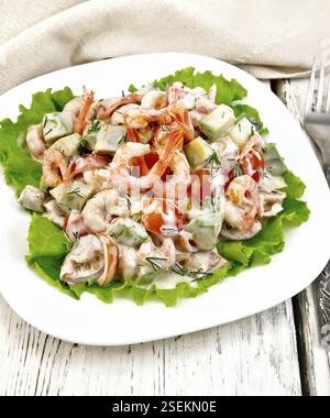 Salat mit Garnelen, Avocados, Tomaten und Mayonnaise auf den grünen Salat auf einen Teller, Servietten, Gabel auf dem Hintergrund der Holzbretter Stockfoto