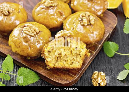 Kleine Kürbis-Cupcakes mit orangefarbener Glasur und Walnüssen, Minze-Zweige auf Holzbrett-Hintergrund Stockfoto
