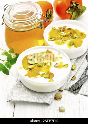 Dessert Joghurt, Dattel und Honig mit Vanille, Kardamom und Pistazien in zwei Schüsseln auf eine Serviette, Minze und Löffel auf dem Hintergrund der hellen Holzmöbeln bo Stockfoto