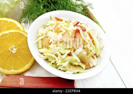Frischer Kohl, Karotten und Rhabarber Salat mit Orangensaft, Honig und Mayonnaise Dressing in einer Platte auf eine Serviette, Dill und Gabel auf weißem Holz- board b Stockfoto