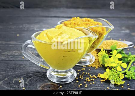 Senf Sauce und Dijon Senf in zwei Töpfe, gelbe Blüten und Samen in einem Löffel auf dem Hintergrund der dunklen Holz- Board Stockfoto