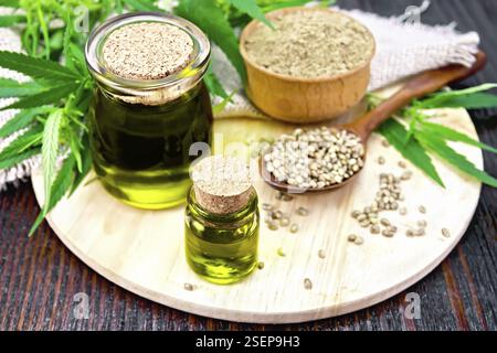 Hanf Öl in zwei Gläsern, Korn in einem Löffel Mehl in eine Schüssel, Blätter und Stängel von Cannabis, eine Serviette von sackleinen auf einem Holzbrett Hintergrund Stockfoto