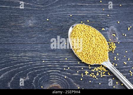 Senfkörner in einem metalllöffel auf dem Hintergrund einer Holzplatte von oben Stockfoto