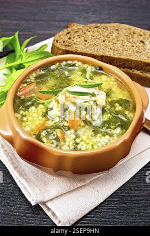 Schweinerippensuppe mit Couscous und Spinat in einer Tonschale auf Küchentuch, Brot auf Holzbretthintergrund Stockfoto