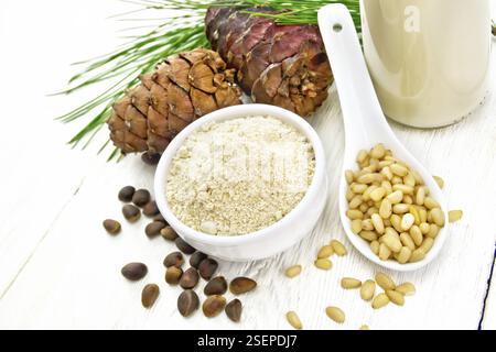 Zedernmehl in einer Schüssel, Nüsse und Kegel, ein Löffel mit geschälten Nüssen, Kiefernzweig und Zedernmilch in einer Flasche auf Holzbrettgrund Stockfoto