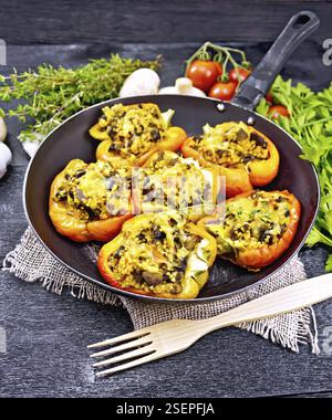 Paprika süss, gefüllt mit Pilzen, Tomaten, Couscous und Käse in eine alte Pfanne auf Sackleinen, eine Gabel, Petersilie und Thymian vor dem Hintergrund o Stockfoto