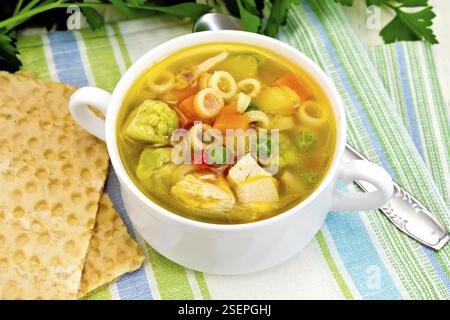 Minestrone mit Fleisch, Sellerie, Tomaten, Zucchini, Kohl, Erbsen, Karotten und Pasta in einer Schüssel auf einem Handtuch auf dem Hintergrund einer Holz- br Stockfoto