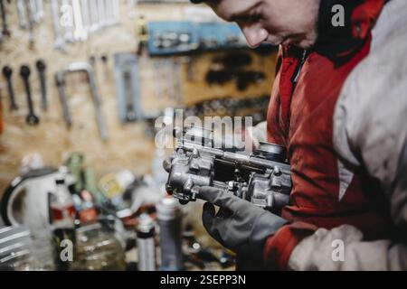 Mechaniker, der einen Vergaser hält und inspiziert, umgeben von Werkzeugen Stockfoto