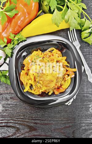 Huhn mit Tomaten, gelben und roten Paprika und Käse in einem Teller auf Serviette, Thymian, Petersilie und Knoblauch auf Holzbrett Hintergrund aus a geschmort Stockfoto