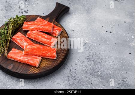 Krabbenstangen, Krabbenfleisch auf Holzbrett. Grauer Hintergrund. Draufsicht. Stockfoto