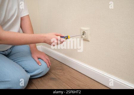 Handreparatur der Steckdose mit einem Schraubendreher an der beigefarbenen Wand. Hauswartung und elektrisches Arbeitskonzept Stockfoto