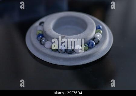 Prozess der Herstellung von handgefertigten Armbändern aus natürlichen organischen Materialien, Perlen und Stein. Eine runde, graue Marmorschale sitzt auf einer dunklen Oberfläche mit blauem, grauem Grau Stockfoto