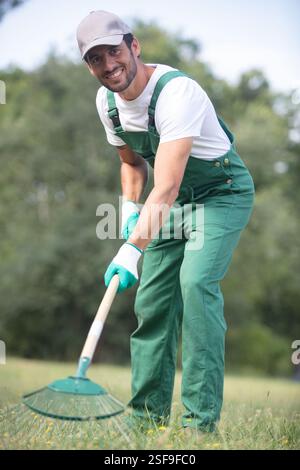 Lächelnder männlicher Gärtner, der Gras harkt Stockfoto