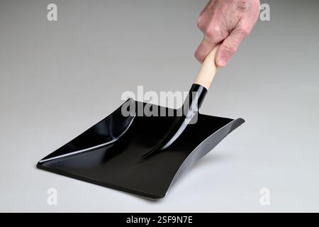 Neuer und sauberer schwarzer Metallstaubbehälter, der von Mann Hand in Studio-Licht auf weißem Hintergrund gehalten wird Stockfoto