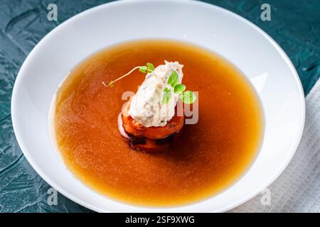 Suppe oder Consomme, dicke Fleischbrühe mit Karotten, Hühnerknödel und Mikrogrün, serviert auf einem weißen Teller auf dunkelgrünem Hintergrund. Hohe Qualität p Stockfoto