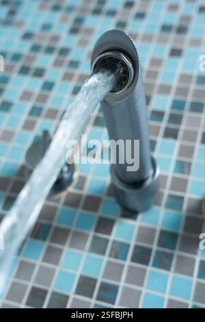 Badezimmermischer, Wasserhahn, fließendes Wasser von unten gesehen in einem englischen Badezimmer mit gefliester Wand. Konzept: OFWAT, Wasserrechnungen, Wasserverbrauch, Wasserverschwendung, Leck Stockfoto