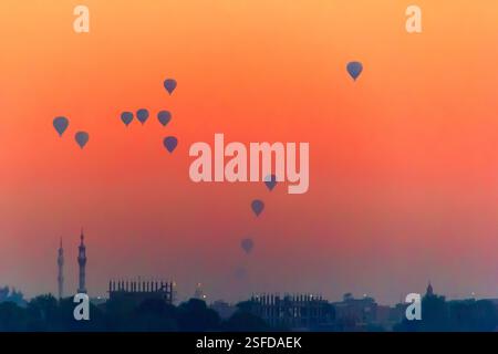 Silhouette von Heißluftballons, die bei Sonnenaufgang über der Skyline der Stadt fliegen, Luxor, Ägypten Stockfoto