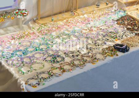 Große Auswahl an bunten, handgefertigten Blumenkronen und Perlen-Accessoires, die auf einem Tisch auf einer Handwerksmesse ordentlich angeordnet sind. Die Pastelltöne und die komplizierten de Stockfoto