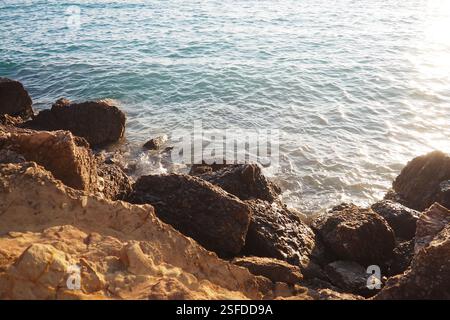 Wellen krachen sanft gegen die zerklüfteten Felsen, während die Sonne über dem Horizont untergeht. Erleben Sie die ruhige Schönheit dieses Küstenortes voller Stockfoto