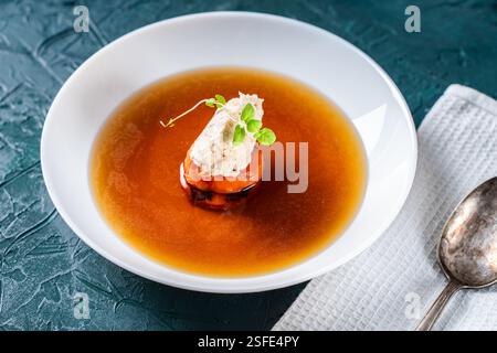 Suppe oder Consomme, dicke Fleischbrühe mit Karotten, Hühnerknödel und Mikrogrün, serviert auf einem weißen Teller auf dunkelgrünem Hintergrund mit Serviette A Stockfoto