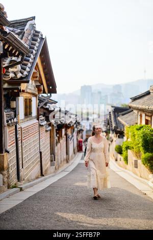 Frau, die durch das Dorf Bukchon Hanok spaziert, mit traditionellen koreanischen Häusern (Hanoks) vor dem Hintergrund moderner Stadtarchitektur in der Ferne Stockfoto