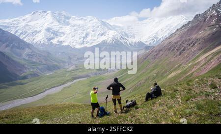 Wanderer genießen die Aussicht auf das grüne Alpental mit den massiven Gletschern des Pamir-Gebirges in Kirgisistan Stockfoto