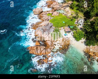 Blick aus der Vogelperspektive auf den Strand von Anse Caiman auf La Digue, Seychellen mit zerklüfteten Granitfelsen, türkisfarbenem Wasser und einem abgeschiedenen Stück Sandküste Stockfoto